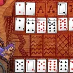 Układ kart w pasjansie na tle drewnianego stołu z ozdobnym wzorem i motywem serca w lewym dolnym rogu