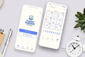Dwa smartfony z aplikacją Sudoku na ekranach, otoczone zegarem, długopisami i rośliną