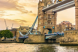 Tower Bridge w Londynie o zachodzie słońca, z widocznymi wieżami i fragmentem mostu, oraz zabudowania w tle