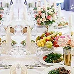 Elegancko nakryty stół z białymi obrusami, udekorowany świeżymi kwiatami, świecami i talerzami z owocami oraz warzywami