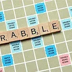 Płytki z literami układające słowo SCRABBLE na planszy z kolorowymi premiami punktowymi