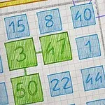 Kolorowe numery w kwadratowych polach na tle z kartki w kratkę, z dwoma centralnymi polami wyróżnionymi na zielono